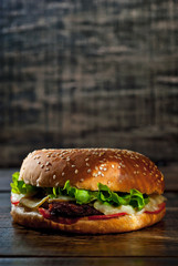 Burger on a dark wooden board. Cheeseburger with cutlet and herbs on black background. Food with contrasting dramatic light. Free space for text.