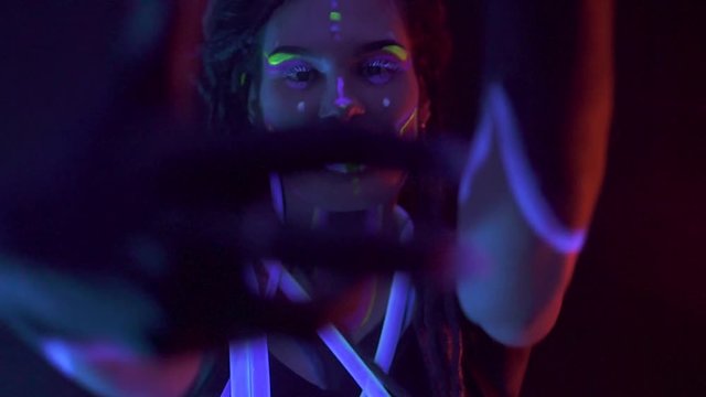 Portrait of a Girl with Dreadlocks in Neon UF Light. Model Girl dancing with glowing tubes with Psychedelic MakeUp, Art Design of Female Disco Dancer Model in UV, Colorful Abstract Make-Up.