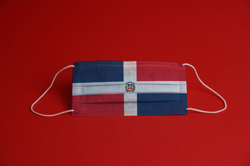 Obraz premium Coronavirus protective mask. Medical mask combined with the Dominican Republic flag. Red background. Face mask protection against pollution, virus, flu. Healthcare and surgery concept.