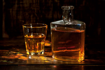 A glass of alcohol near a bottle. Old whiskey bottle on black wooden table. Drinks on a dark blurred background.