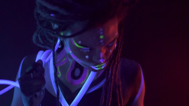 Portrait of a Girl with Dreadlocks in Neon UF Light. Model Girl dancing with glowing tubes with Psychedelic MakeUp, Art Design of Female Disco Dancer Model in UV, Colorful Abstract Make-Up.