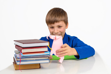 child development, origami: a schoolboy boy in a blue T-shirt sits at the table and plays with an elephant from paper, next to a stack of textbooks