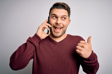 Young man with blue eyes speaking on the phone having a conversation on smartphone pointing and showing with thumb up to the side with happy face smiling