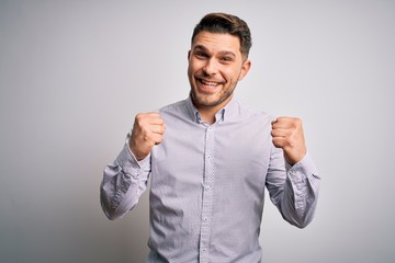 Young business man with blue eyes standing over isolated background celebrating surprised and...