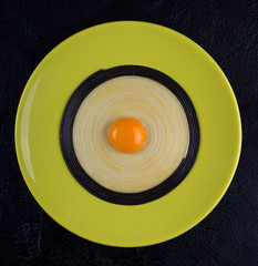 Olive color plate with black and white linguini pasta with egg yolk in the middle over on black background. Minimalistic style