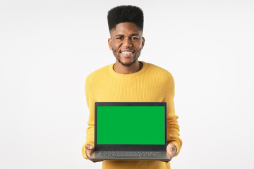 Cheerful young african american guy in casual posing isolated on white background holding laptop computer with mockup screen