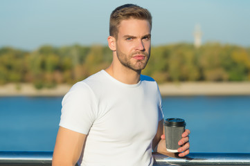 Takeaway coffee is my lifestyle. Handsome man hold coffee cup outdoors. Young guy drink coffee on summer morning. Enjoying coffee on river bank