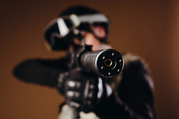 Soldier with gun is looking through the scope on brown background. Concept of war. Veterans, comrades, soldiers. Man in uniform.