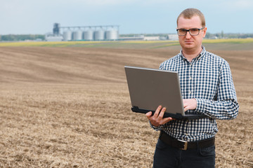 modern farmer checking his field plant and working on laptop computer against corn dryer silos in concept of industrial and agriculture © Serhii