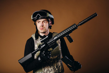 Soldier with gun inserts magazine with cartridges on brown background. Concept of war. Veterans,...