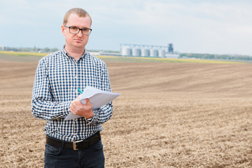 modern farmer checking his field plant against corn dryer silos in concept of industrial and agriculture © Serhii
