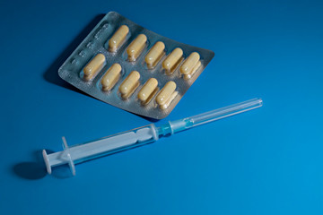 capsules in a transparent blister and a syringe with a needle on a blue background. There is space...