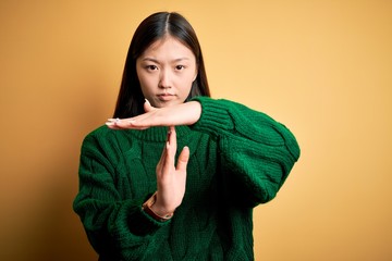 Young beautiful asian woman wearing green winter sweater over yellow isolated background Doing time...