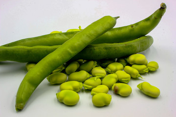  open green broad beans in their shells and some shelled beans isolated on a white background