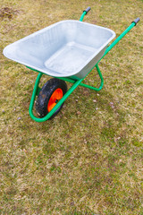 Garden metal wheelbarrow with green reinforced frame on one wheel in the garden