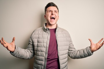 Young handsome caucasian man wearing casual winter jacket standing over isolated background crazy and mad shouting and yelling with aggressive expression and arms raised. Frustration concept.
