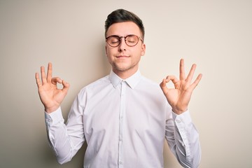 Young handsome business mas wearing glasses and elegant shirt over isolated background relax and smiling with eyes closed doing meditation gesture with fingers. Yoga concept.