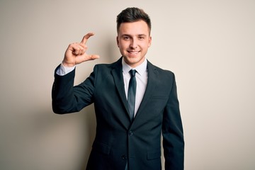 Young handsome business man wearing elegant suit and tie over isolated background smiling and confident gesturing with hand doing small size sign with fingers looking and the camera. Measure concept.