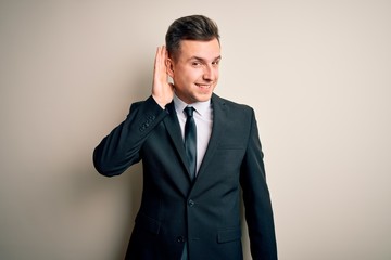 Young handsome business man wearing elegant suit and tie over isolated background smiling with hand over ear listening an hearing to rumor or gossip. Deafness concept.