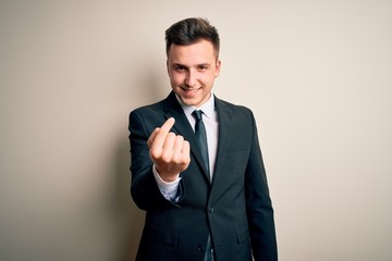 Young handsome business man wearing elegant suit and tie over isolated background Beckoning come here gesture with hand inviting welcoming happy and smiling
