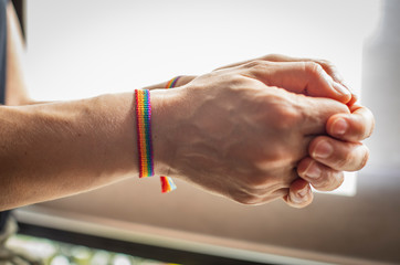 Different postures of hands with a bracelet with the flag GAY-LGTB on a yellow and white...