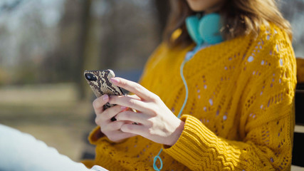 Young girl with headphones using phone in a city park.