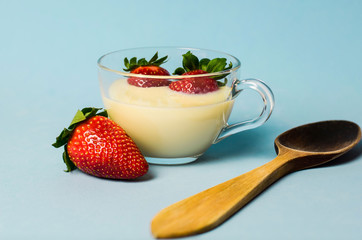 Cup of condensed milk with strawberries next to a wooden spoon on blue background
