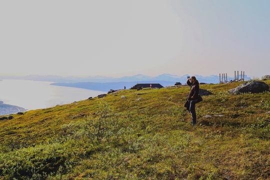 Side View Of Man Shielding Eyes On Grassy Mountain Against Clear Sky