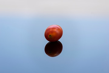 A red cherry tomato on a blue glass surface