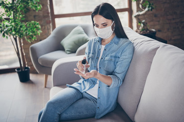 Portrait of serious girl sit divan corona virus infection want prevent bacteria germ spreading use sanitizer spray hands skin wear medical mask in house indoors