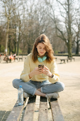 Young girl with headphones using phone in a city park.