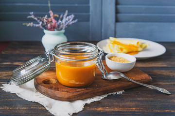 Homemade fresh caramel sauce in glass jar, brown sugar on wooden board, rustic table. Country...