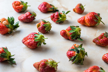 Ugly fresh ripe strawberries lie on a marble table. Natural berries with flaws and strange, unusual shapes. Berries lie one at a time evenly filling the table, pattern.