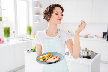 Photo of pretty housewife lady chef hold ready grilled salmon trout fillet steak roasted condition with garnish cook dinner one person portion wear apron t-shirt modern kitchen indoors