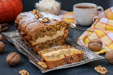 Homemade pumpkin muffin with cottage cheese and walnuts, sprinkled with icing sugar and cup of tea against a dark background, selective focus