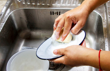 Woman hands without gloves cleaning dishes with sponge and dishwashing liquid.