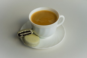 View of white coffee cup full with black coffee together with round cookies enrobed with white chocolate standing on a white plate at kitchen