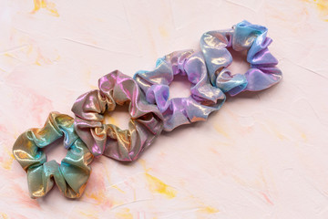 Four trendy holographic iridiscent shiny metallic scrunchies on pink background. Diy accessories...