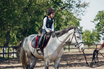 Little Girl in helmet Learning Horseback Riding. Instructor teaches kid Equestrian.