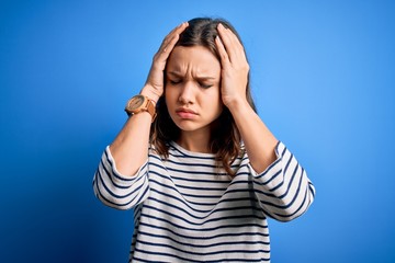 Young beautiful blonde girl wearing casual sweater standing over blue isolated background suffering from headache desperate and stressed because pain and migraine. Hands on head.