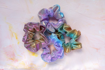 Four trendy holographic iridiscent shiny metallic scrunchies on pink background. Diy accessories and hairstyles concept, copy space