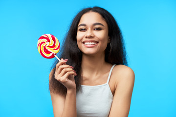 Happy beautiful black woman with colorful lollipop on blue background