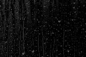 Naklejka na ściany i meble Drops of water flow down the surface of the clear glass on a black background. 