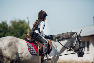 Little Girl in helmet Learning Horseback Riding. Instructor teaches kid Equestrian.