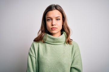 Young beautiful blonde girl wearing winter sweater standing over isolated background with serious...