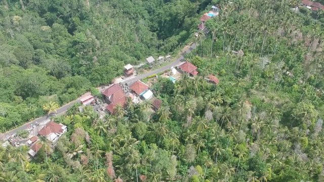 span over the road with houses with red roofs running along the ridge all around in the thickets of Cotinus coggygria and palm trees in sunny weather bali indonesia