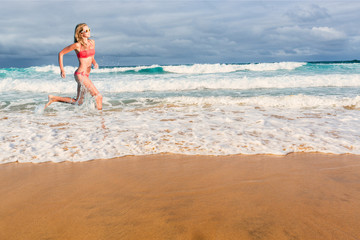 Beautiful blonde woman in bikini running in the water on tropical beach. Portrait of happy young sporty woman.