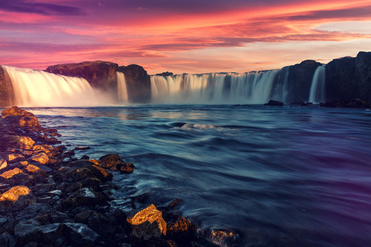 Colorful summer landscape of Iceland. Majestic Godafoss waterfall with picturesque dramatic sky, during sunset. Scenic image of Icelandic nature.  Popular travel and hiking destination