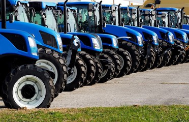 Fototapeta premium Close up of brand new blue tractors, side by side, in a long line
