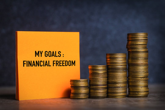 My goals and financial freedom written on orange note paper and coins stack